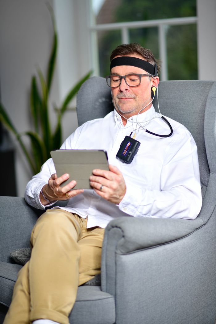 Man sitting in armchair using a neurofeedback device with tablet indoors.