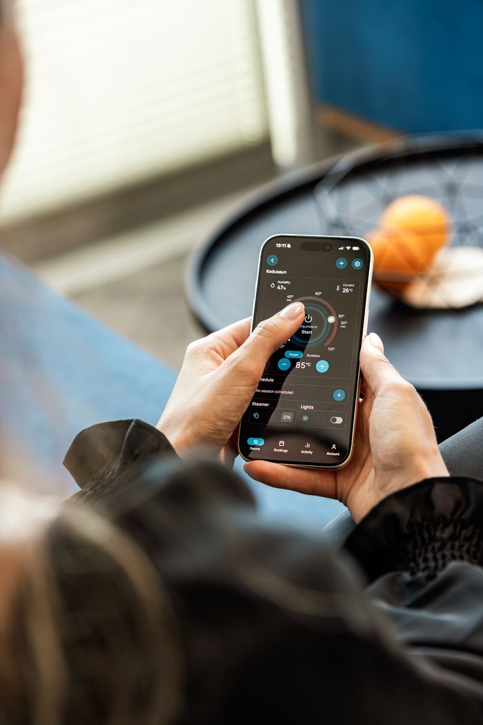 A woman uses a smartphone app to adjust settings for a home sauna, showcasing modern technology in wellness.